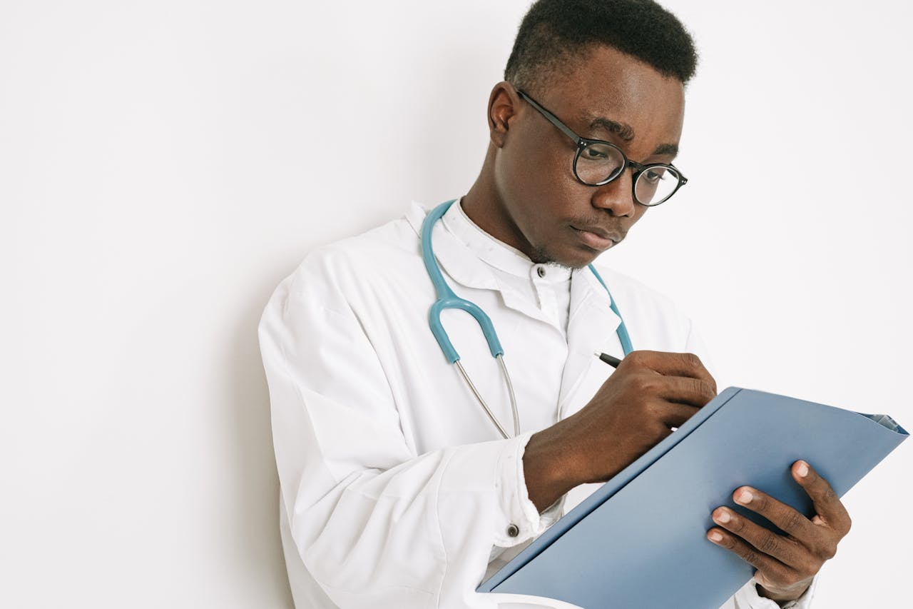 A focused doctor takes notes on a clipboard while wearing a medical gown and stethoscope.